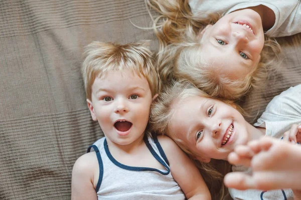 Retrato de tres niños acostados en la cama. Hermanas y hermano sonriendo mientras miran a la cámara —  Fotos de Stock