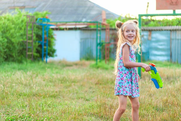 Little girls play in the summer on a green meadow with water pistols — Stockfoto