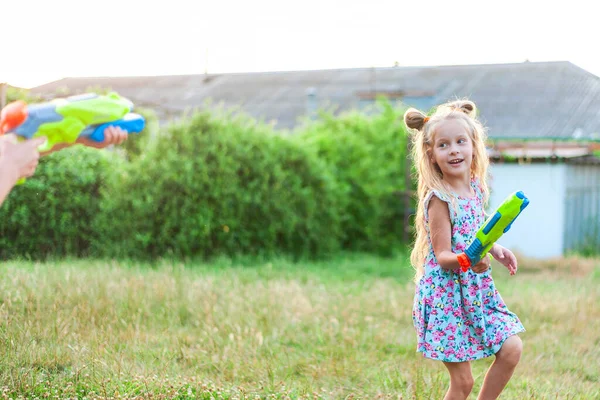 Little girls play in the summer on a green meadow with water pistols — Stockfoto
