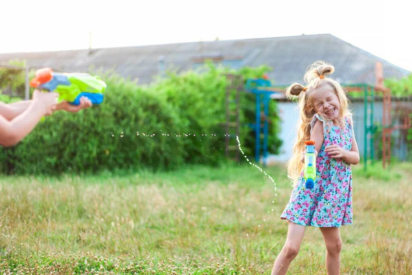 Zwei kleine Mädchen spielen im Sommer auf einer grünen Wiese mit Wasserpistolen — Stockfoto