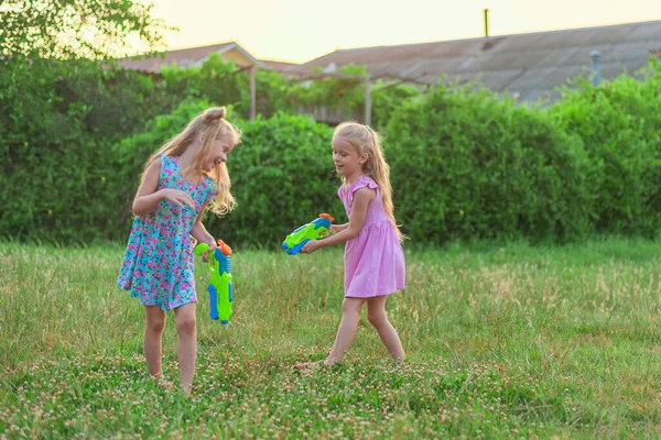 Zwei kleine Mädchen spielen im Sommer auf einer grünen Wiese mit Wasserpistolen — Stockfoto