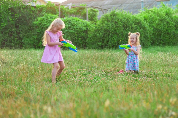 Zwei kleine Mädchen spielen im Sommer auf einer grünen Wiese mit Wasserpistolen — Stockfoto