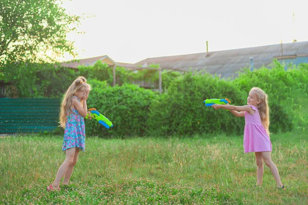 Két kislány játszik nyáron egy zöld réten vízipisztollyal — Stock Fotó