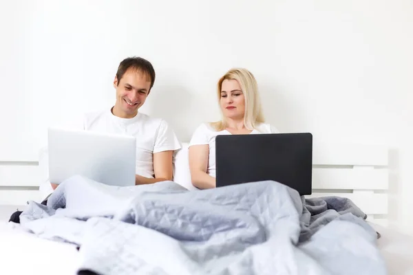 man and woman sitting on bed in morning having fun, laughing, working on laptop onile education, online freelancer job, smiling happy, family living together, bedroom, wearing pajamas