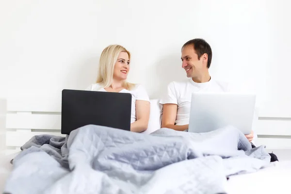 man and woman sitting on bed in morning having fun, laughing, working on laptop onile education, online freelancer job, smiling happy, family living together, bedroom, wearing pajamas