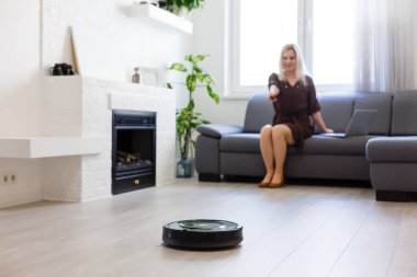 Kadın kanepede dinlenirken robot süpürgesi odayı temizliyor.