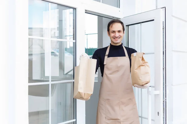 エプロンを着た顔の毛をした笑顔の若い男の肖像画とカフェでバーカウンターにもたれています テキストや画像のための空白のスレートボードのコピースペース バーテンダーの所有者のスタッフサービスと居心地の良いコーヒーショップ — ストック写真