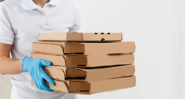 Man from delivery service in t-shirt, in protective mask and gloves giving food order and holding pizza boxes over white background