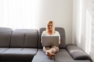 Evde dizüstü bilgisayarının önünde gülümseyen bir kadın.