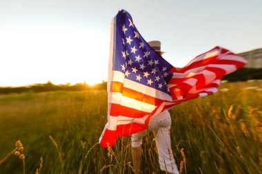 Çavdar tarlasında rüzgarda Amerikan bayrağı tutan güzel bir genç kız. Mavi gökyüzüne karşı yaz manzarası. Yatay yönelim.