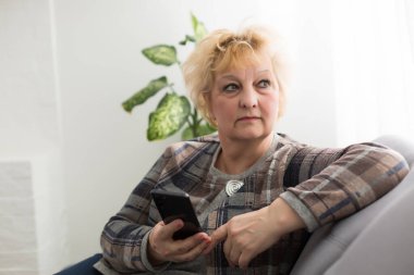 Modern teknolojinin her çağda kolay ve hızlı kullanımı kavramı. Kırışıklıkları olan kendinden emin olgun bir kadının portresi gri arka planda izole edilmiş bir mesaj göndermek için modern akıllı telefonunu kullanıyor.