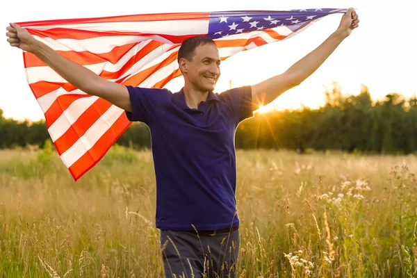 Fourth of July. Patriotic man with the national American flag in the field. Young man proudly waving an American flag. Independence Day.