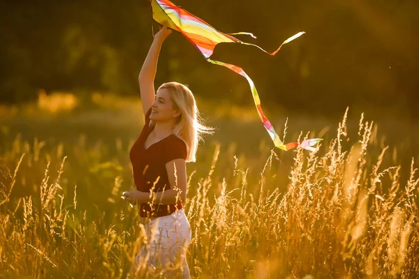 Beauty girl running with kite on the field. Beautiful young woman with flying colorful kite over clear blue sky. Free, freedom concept. Emotions, healthy lifestyle
