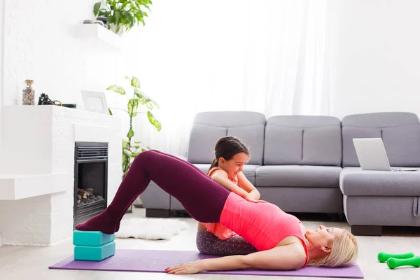 Woman is doing online yoga with laptop during self isolation at her living room, no equipment workout, meditation tips for beginners. Family time with kids, stay home.