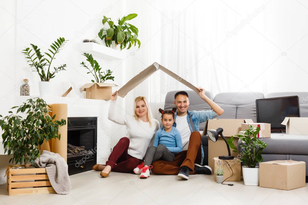 Happy family sitting on wooden floor. Father, mother and child having fun together. Moving house day, new home and design interior concept