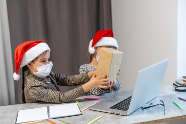 Noel internete düştü. Maskeli iki küçük kız dizüstü bilgisayar izliyor. Noel zamanı kavramı