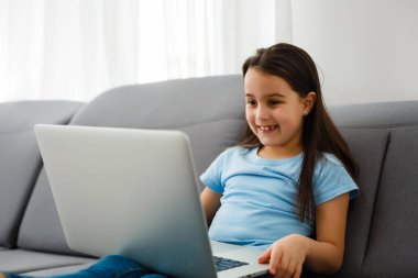 Evde öğrenen mutlu küçük bir öğrencinin portresini yakından çek. Gülümseyen küçük kız oturma odasında ders almaktan zevk alıyor. Zeki kız öğrenci kameraya bakıyor, internetten ders çalışıyor..