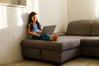 Uzaktan eğitim. Çocuk mutlu bir şekilde gülümser ve uzaktan bilgi alır. Küçük kız evde bilgisayarla online öğrenim görüyor. Çevrimiçi okul.