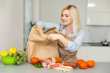 Kendini izole etme kavramı. Mutfakta yiyecek dolu kağıt torbaları boşaltan kadın salgın sırasında karantinaya alınmaya hazır.
