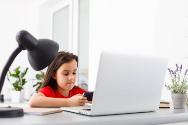 Uzaktan eğitim. Çocuk mutlu bir şekilde gülümser ve uzaktan bilgi alır. Küçük kız evde bilgisayarla online öğrenim görüyor. Çevrimiçi okul.