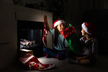 Noel arifesinde sıcak, karanlık bir oturma odasında şöminenin yanında oturan iki küçük kız.