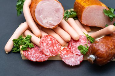 Farklı bir jambon ve salamlı, koyu bir arka planda otlar.