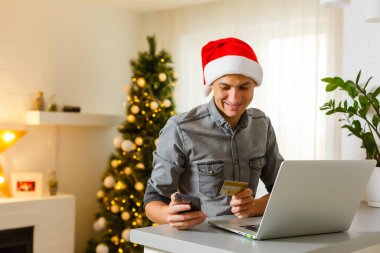Genç adam Noel için evde kredi kartıyla online alışveriş yapıyor. Noel alışveriş konsepti.
