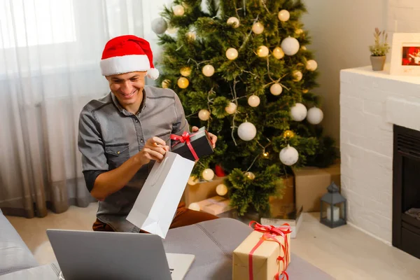 陽気な男がソファに座ってクリスマスツリーの近くのノートパソコンを使って — ストック写真