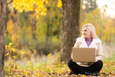 Genç bir kadın dizüstü bilgisayarla parkta oturuyor.