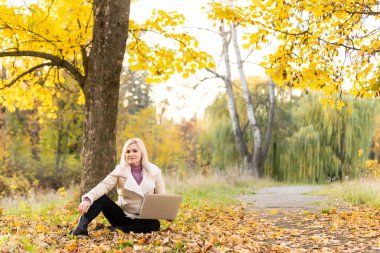 Kadın dizüstü bilgisayarı üzerinde çalışırken parkta dinleniyor.
