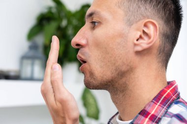 Nefesi kokuyor. Ağız kokusu konsepti. Genç adam elleriyle nefesini kontrol ediyor..