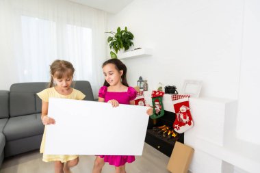 İki küçük kız ellerinde boş bir yatay afiş, bir resim tuvali ile duruyorlar.