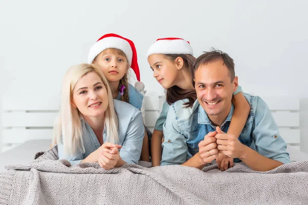 クリスマスファミリーは赤い帽子の白いベッドに横たわっています 幸せな両親と子供 — ストック写真