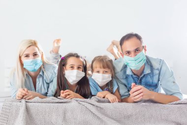 Aile karantinada, ev hapsindeyken koronavirüs, karı koca ve çocuklar yatakta, aile maskeli.
