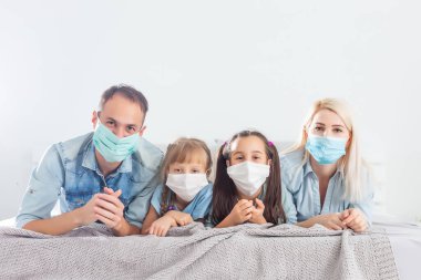 Aile karantinada, ev hapsindeyken koronavirüs, karı koca ve çocuklar yatakta, aile maskeli.