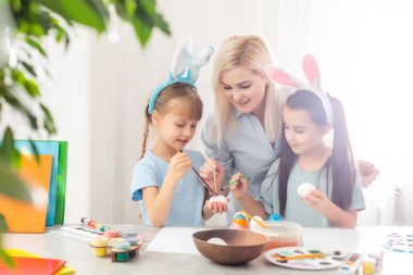 Genç anne ve iki kızı Paskalya yumurtası boyuyor.