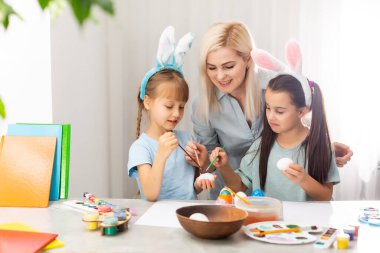 Genç anne ve iki kızı Paskalya yumurtası boyuyor.