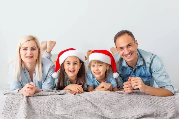 クリスマスファミリーは赤い帽子の白いベッドに横たわっています 幸せな両親と子供 — ストック写真