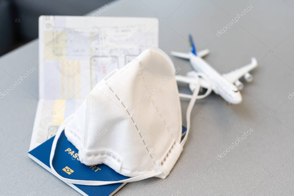 Plane toy, passport, face mask on gray background. Flight cancellation due to the impact of coronavirus COVID-19 concept.