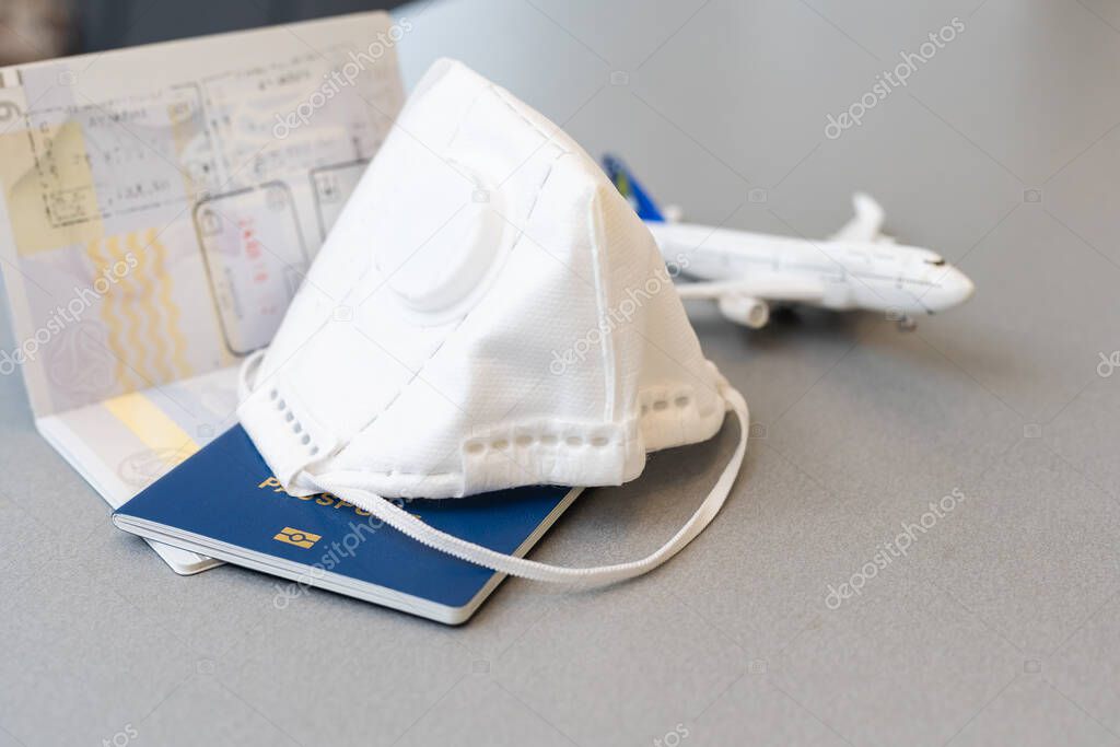 Plane toy, passport, face mask on gray background. Flight cancellation due to the impact of coronavirus COVID-19 concept.