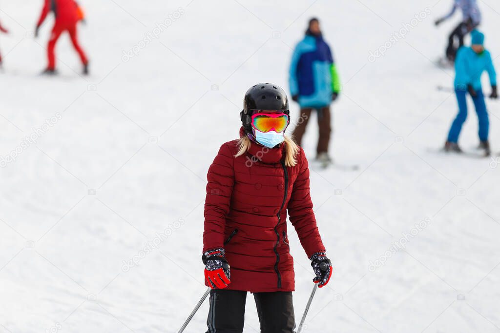 Portrait of a woman skier in medical mask during COVID-19 coronavirus on a snowy mountain at a ski resort