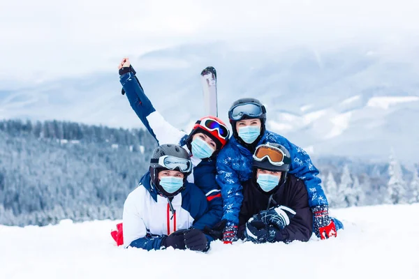 Group of happy friends having fun. Young people with face mask during COVID-19 coronavirus on a snowy mountain at a ski resort