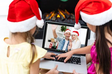 Çevrimiçi yeni normal Noel kutlaması. Çocuklar Noel 'i babalarıyla görüntülü sohbet yoluyla kutlamak için dizüstü bilgisayar kullanıyorlar. Mutlu tatiller, açık havada.