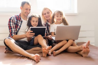 Aile dizüstü bilgisayar kullanarak yatakta yatıyor.