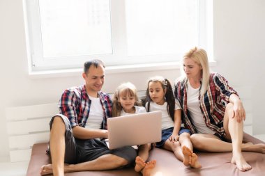 Aile dizüstü bilgisayar kullanarak yatakta yatıyor.