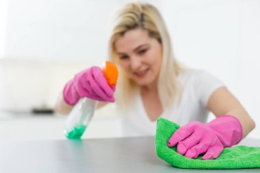 Temizlik moda haline geldi. Güzel, gülümseyen bir kadın. Masayı kumaş ve özel yıkama araçlarıyla siliyor.