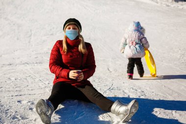 Güneşli bir kış gününde, COVID-19 Coronavirus sırasında tıbbi maske takan bir kadın.