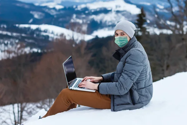 medical mask as protection against coronavirus. guy in the mountains isolated from coronavirus. works on laptop