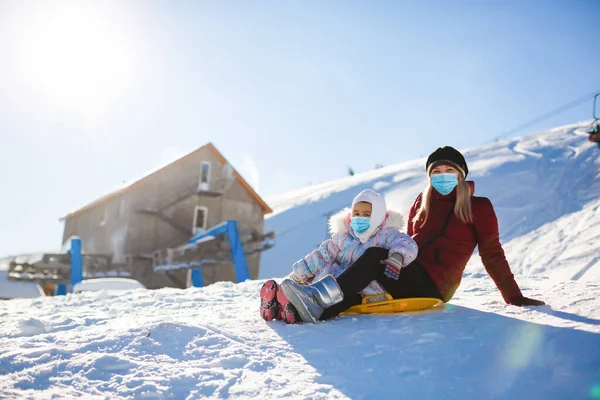 family wearing a medical mask during COVID-19 coronavirus on a snowy mountain at a ski resort