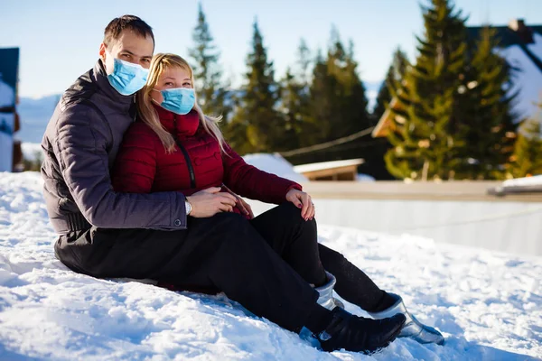 family wearing a medical mask during COVID-19 coronavirus on a snowy mountain at a ski resort